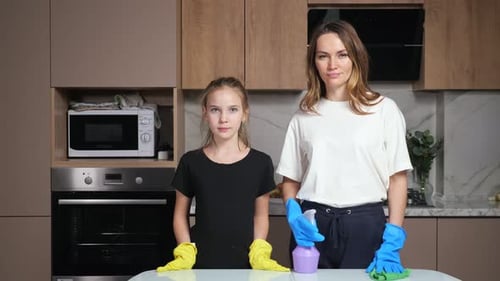 Mother and Daughter with Gloves Stand Near Table in Kitchen