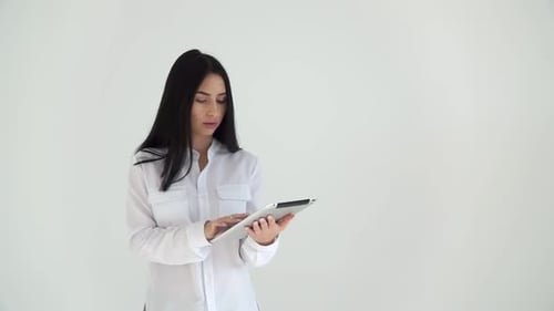 The Girl Flips Through the Tablet, Thoughtfully Tucks Her Hair Behind Her Ear. The Designer Works in