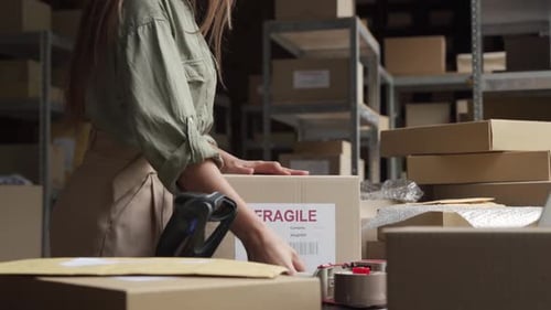 Female Post Mail Storage Worker Holding Tape Dispenser Sealing Shipping Box