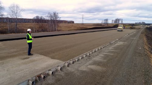 Trabalhador em um capacete branco e colete, fica com um tablet na construção da estrada