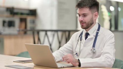 Pensive Young Doctor Thinking and Working on Laptop in Office
