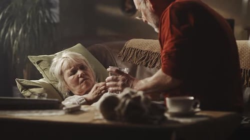 Senior Woman Drinking Water with Help from Companion