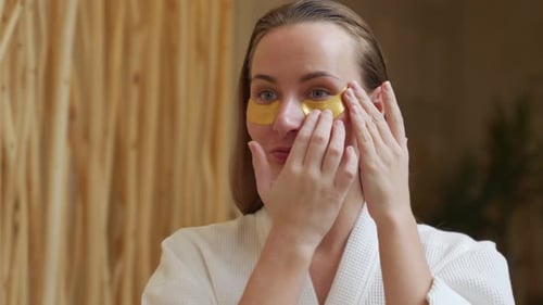 Woman Applying Gold Eye Patches in Bathroom