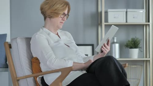 Old Senior Woman Browsing Internet on Tablet PC, Sitting on Couch