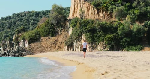 Slow Motion Footage of the Man in Blue Shorts and a White Tshirts Walks on a Deserted Beach He Moves