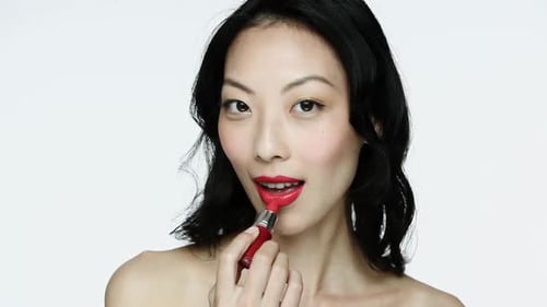 Woman Applying Beautiful Red Lipstick in Studio