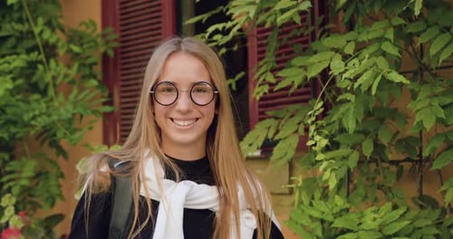 Jeune fille aux lunettes élégantes debout devant la caméra près d'un ancien bâtiment de la ville