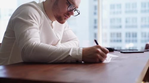 Young Adult Man Writing on Paper at Desk