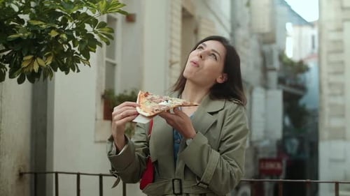 Pretty young women in green coat eating pizza outdoors on the terrace in spring time