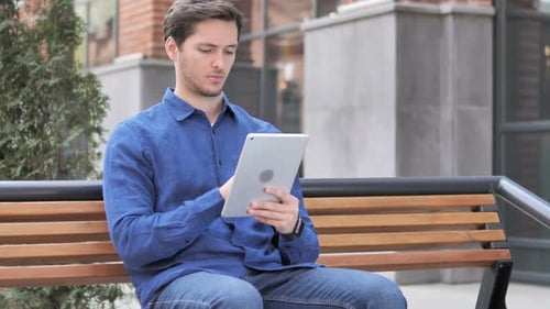 Junger Mann benutzt Tablet beim Sitzen auf der Bank