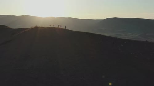 A Group of Travelers Walk Along the Top of the Hill Against the Backdrop of the Mountains of the