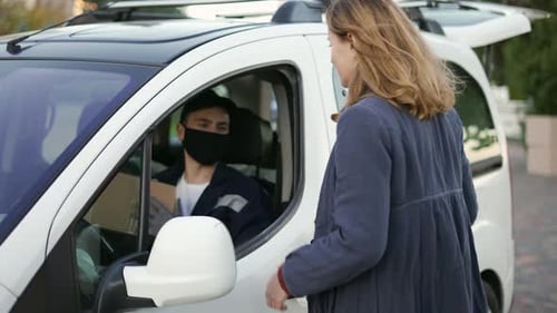Zusteller mit einheitlicher Schutzmaske und Handschuhen übergibt dem Kunden ein Paket auf der Ladung