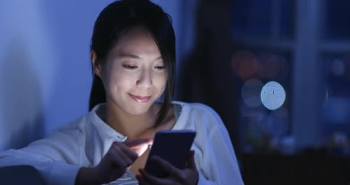 Smiling Woman Using Phone at Night Indoors
