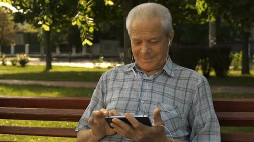 Senior Man Uses Smartphone and Listens to Music in Park