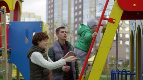 Junge klettert am Spielplatz Leiter hinauf und Eltern bewachen