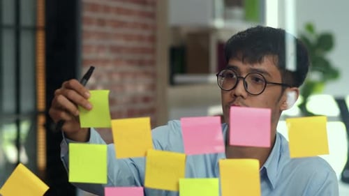 Asian creative man stick a sticky note on glass board.
