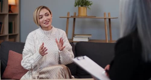 Ausschnittansicht einer fröhlichen Frau mit kurzen blonden Haaren, die mit einem Therapeuten im Büro spricht