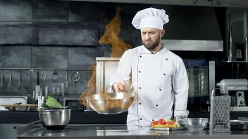 Professioneller Koch wirft Essen in die Pfanne mit brennender Flamme in die Küche