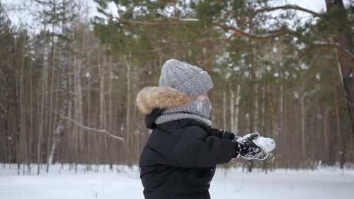 Der Junge wirft etwas Schnee in die Luft und genießt die kalte Jahreszeit in Zeitlupe.