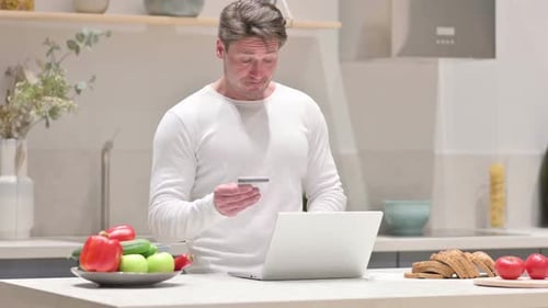 Man using Laptop with Credit Card in Kitchen