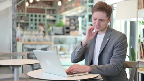 Young Adult Working on Laptop Rubs Neck in Cafe