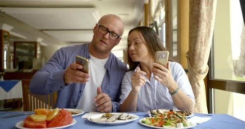 Adults Using Smartphones Together at Restaurant Table