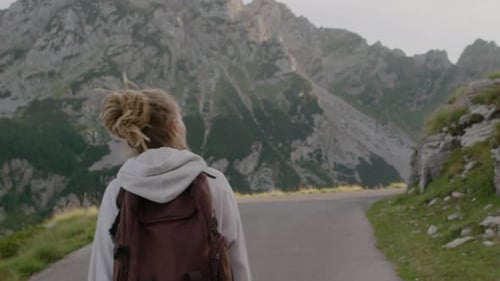 Back view of travel woman with dreadlocks and backpack walking through the national park