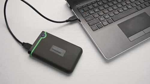 Young Woman Disconnects a Portable Hard Drive From a Laptop Computer Against a Light Background