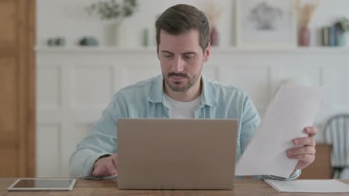 Man working at laptop crumples documents in frustration