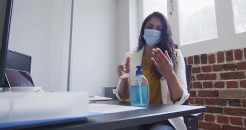 Woman wearing face mask sanitizing her hands at office