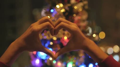 Hands Making Heart Shape in Front of Christmas Tree