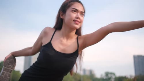 Asian sport woman do yoga posture near lotus pond in green park and look to evening light cityscape