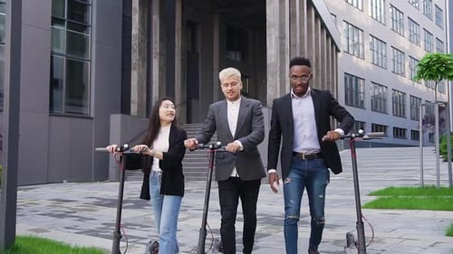 Mixed Race Group of Friends Passing Near Urban Building with Their Electric Scooters and Talking