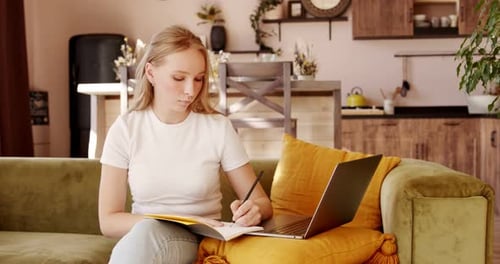 Woman Writes in Notebook With Laptop on Couch