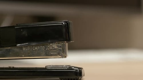 A close up from the side of a black stapler stapling pieces of paper together in slow motion.