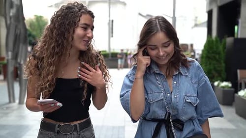 Close-up of Two Fun, Stylish and Friendly Young Women Walking Down a City Street Full of People and