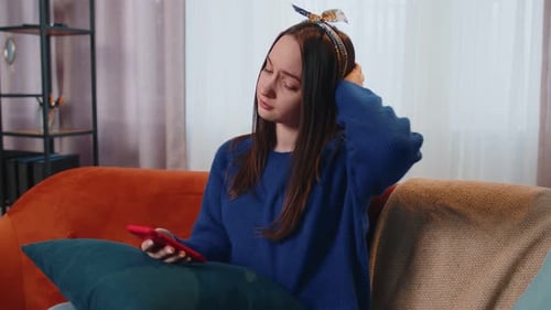 Sad Young Woman on Couch Using Cell Phone