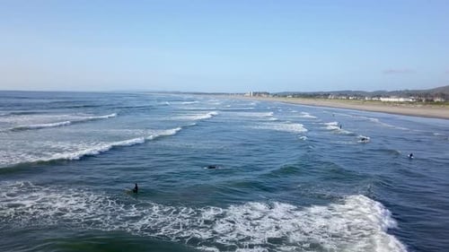 Aerial view of many surfers in the water catching waves in the Pacific Ocean.