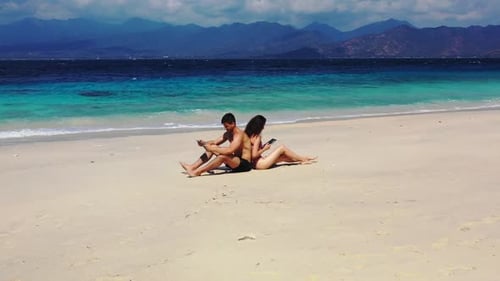 Two lovers tanning on tropical tourist beach break by blue lagoon and clean sand background of Bali