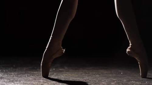Graceful Ballerina Dancing on Her Pointe Ballet Shoes in Spotlight on Black Background in Studio