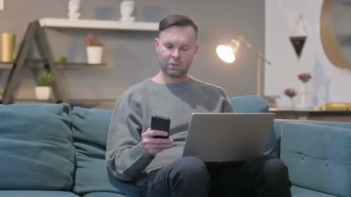 Man With Laptop and Phone Working From Home