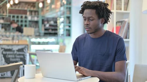 Pensive African Man Working on Laptop in Cafe
