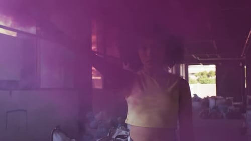 Mixed race woman holding purple flare standing in an empty building