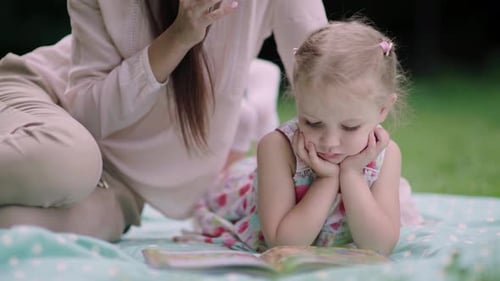 Young Mother And Daughter Reading Book Lying On Grass At Park