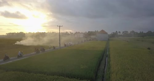 Aerial drone view of farming fields and a road with burning smoke at sunset.