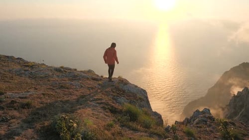 Silhuette of Young Man Arms Outstretched Observing Beautiful Dramatic Colorful Sunset Above a Sea