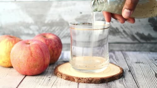 Glass Being Filled with Drink Next to Apples