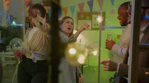 Grupo de empresários dançando com faíscas e champanhe em festa no escritório escuro