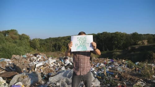 Man Holds Sign at Polluted Landfill Site