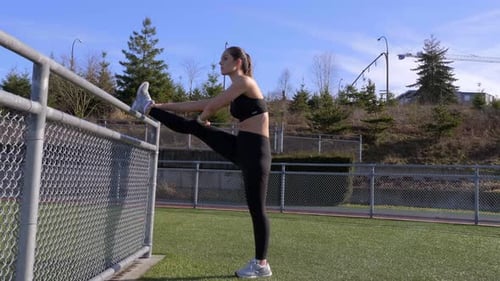 Athletic Woman Stretching Leg on Fence Outdoors